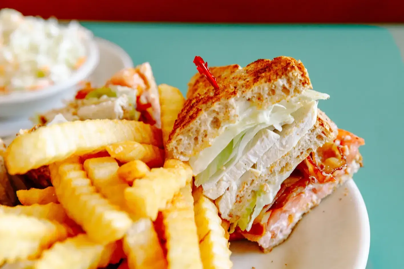 Club sandwich with crinkle-cut fries on a plate, with coleslaw in the background.