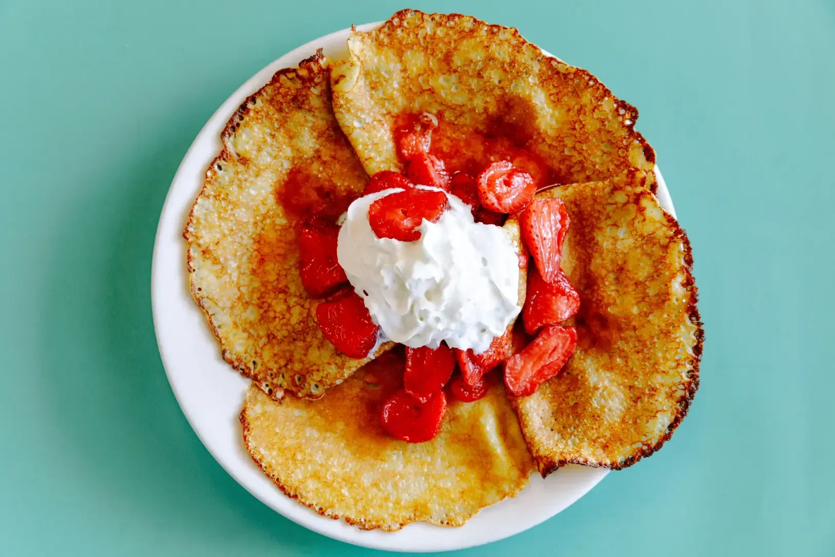 Dessert crepes topped with strawberries and whipped cream on a white plate