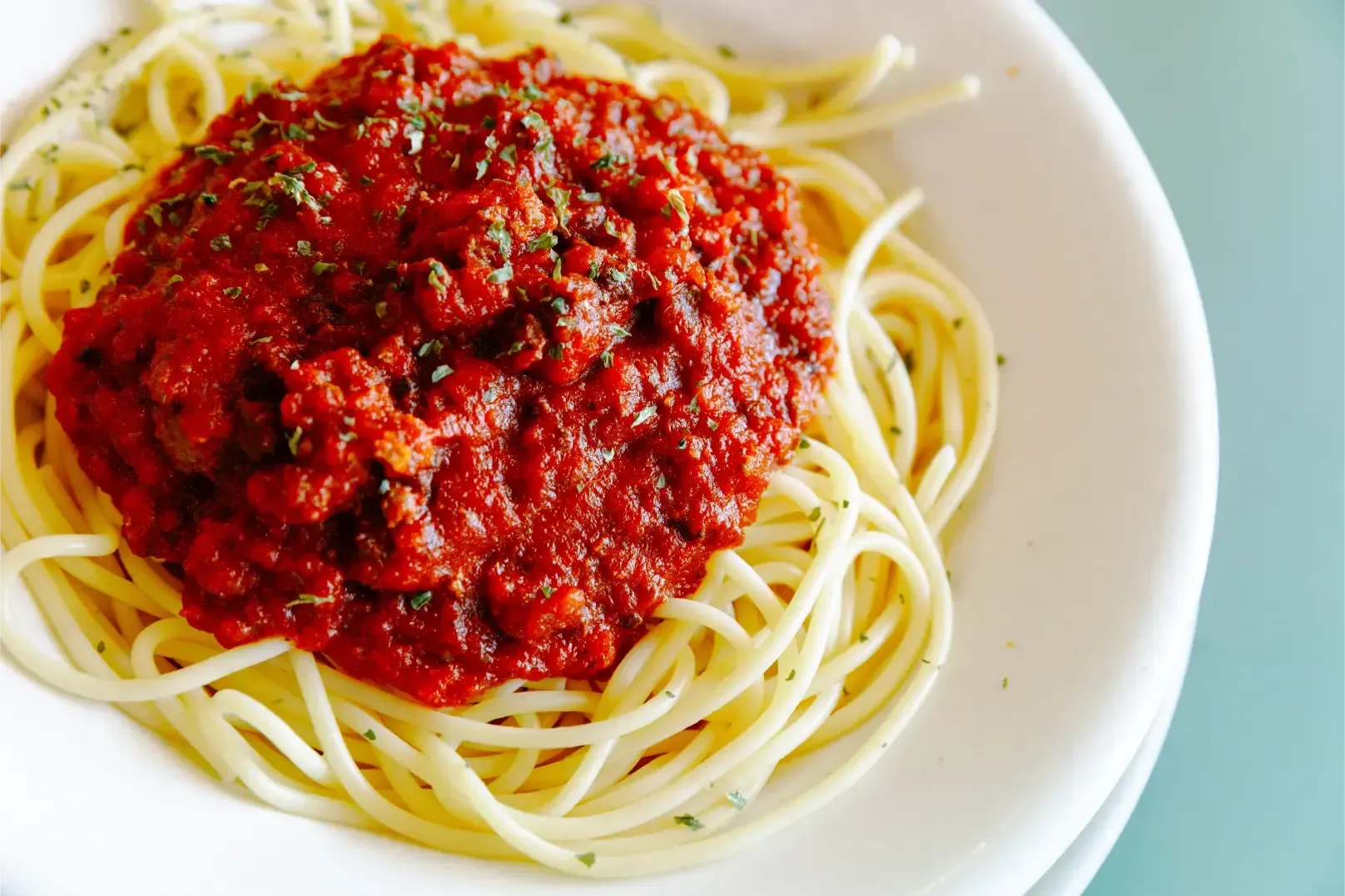 Plate of spaghetti with red tomato sauce and herbs on a white dish