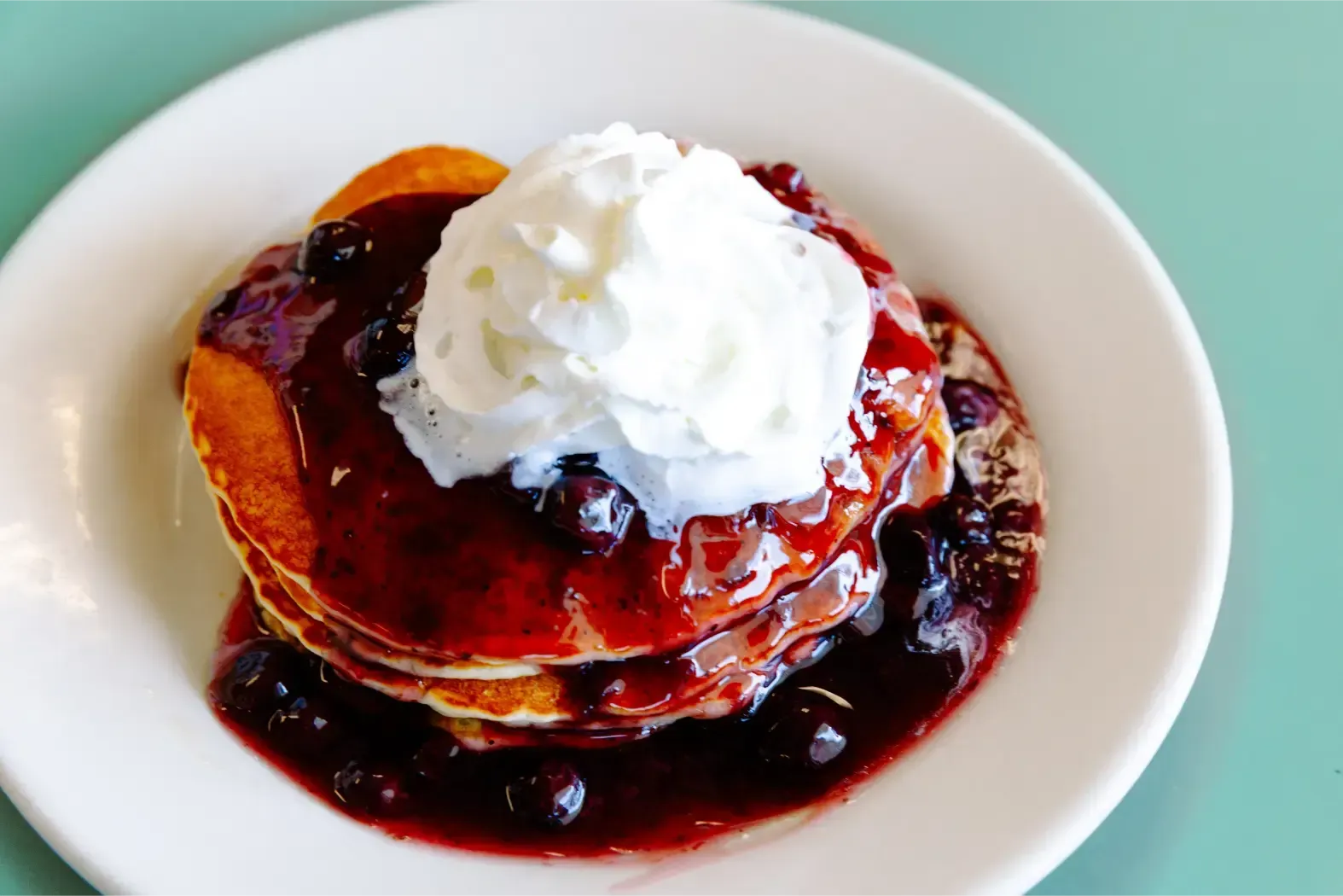 Stack of pancakes topped with whipped cream and berry syrup on a white plate