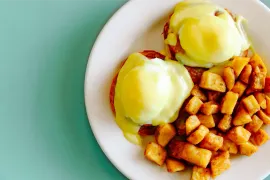 Two poached eggs and diced potatoes on a white plate against a mint green background