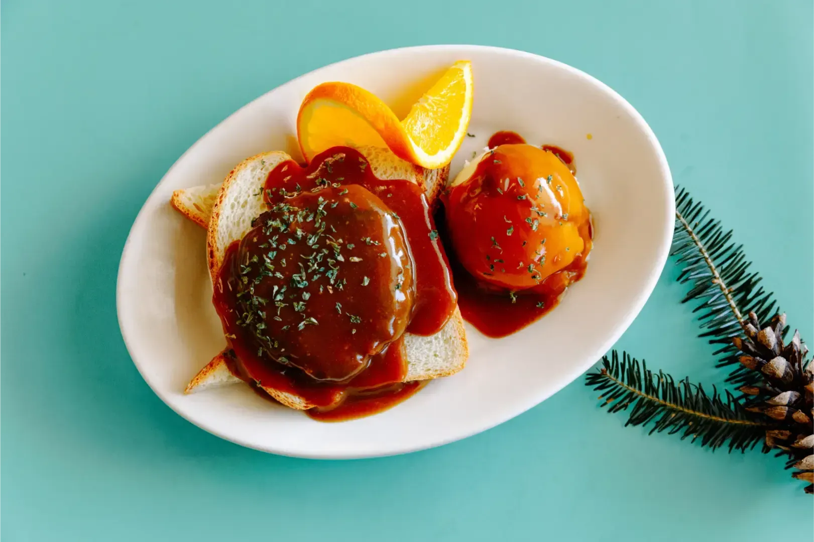 Plate with two sauced pancakes and orange slices on a turquoise background