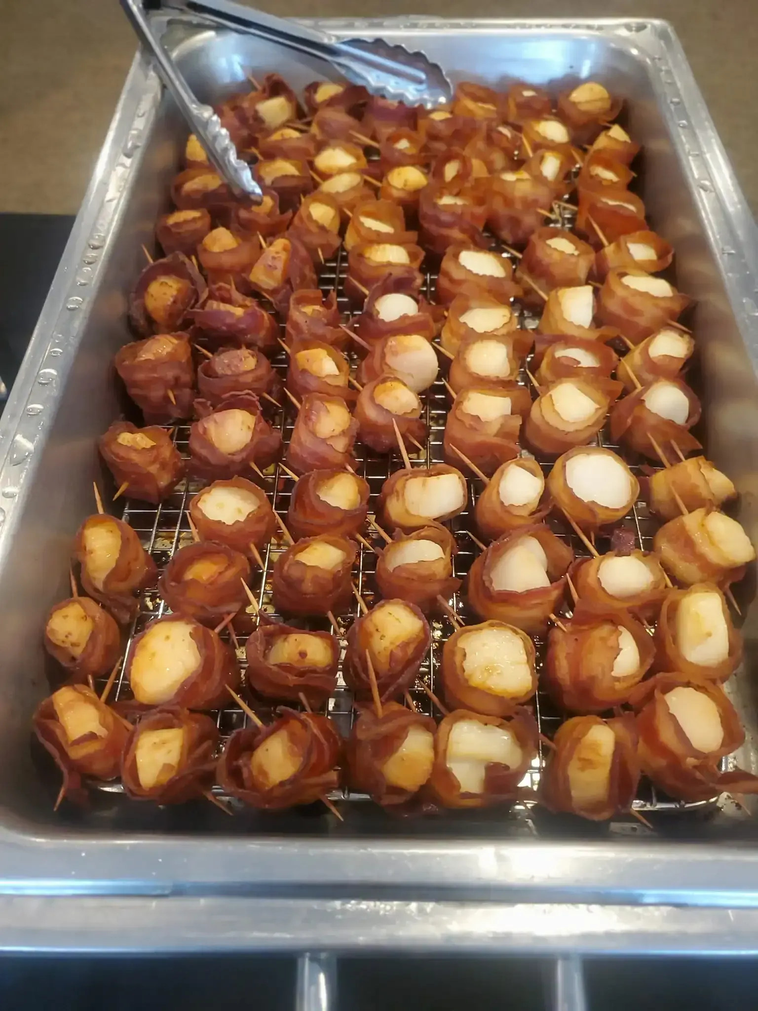 Tray of chocolate-covered cake pops arranged in rows, with metal tongs at the top left.