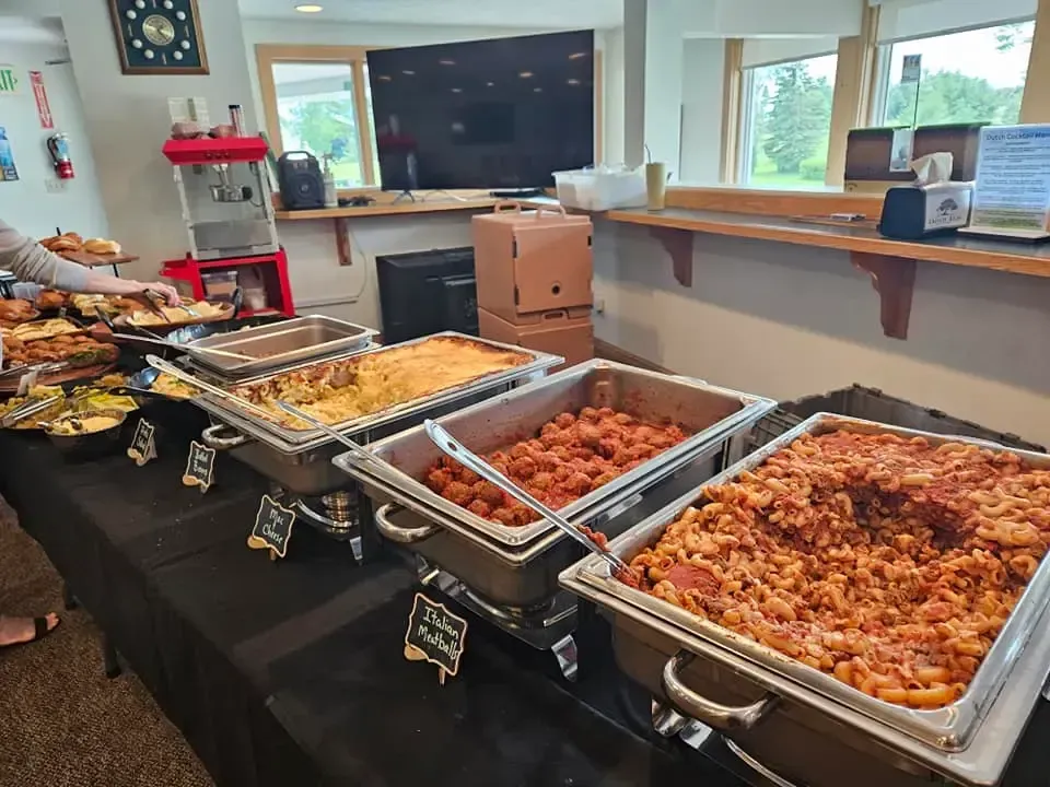 Buffet table with trays of baked dishes in a bright dining room near a windowed counter