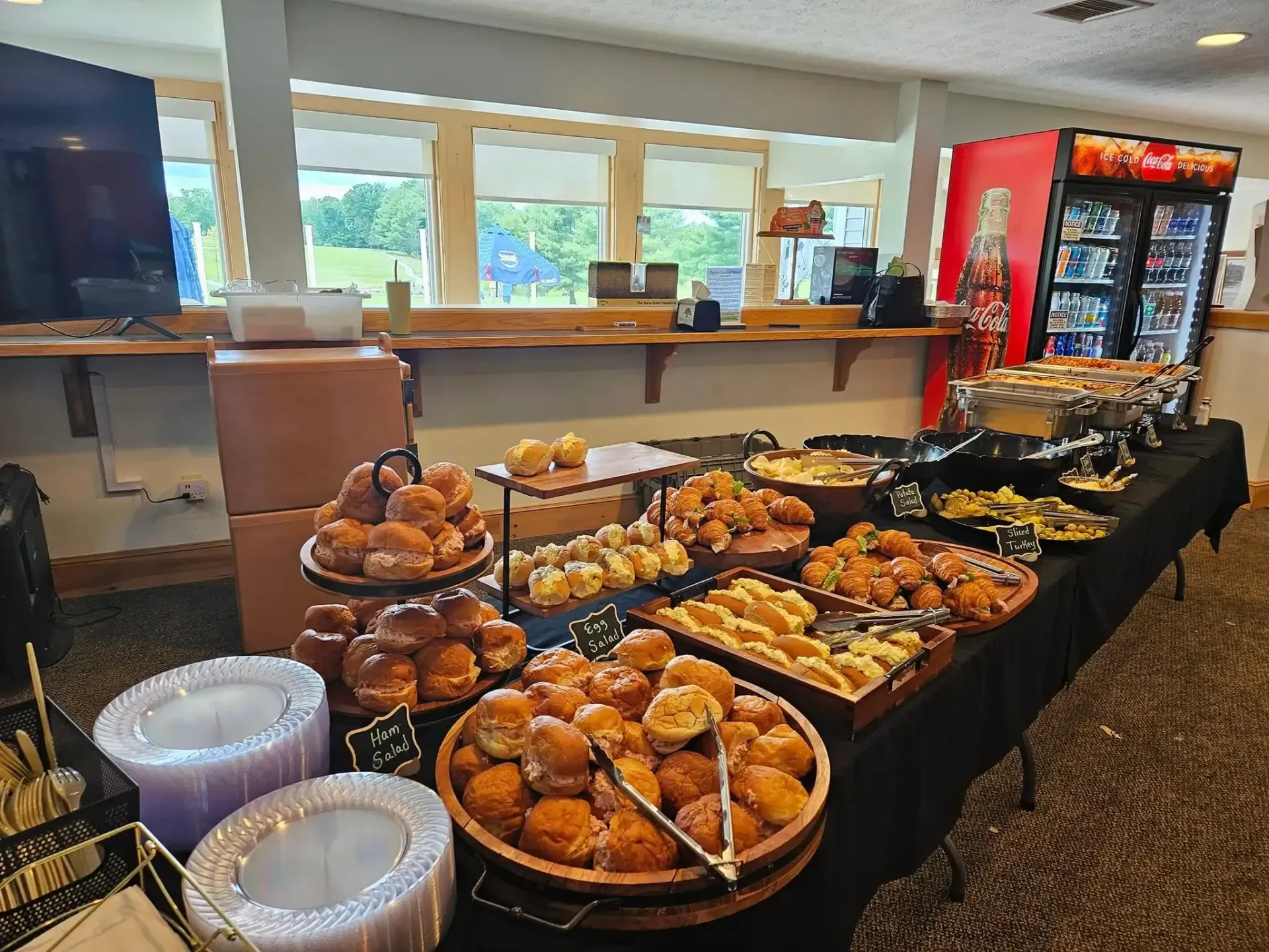 Bakery buffet table with assorted pastries and donuts beside a drink cooler in a bright dining area