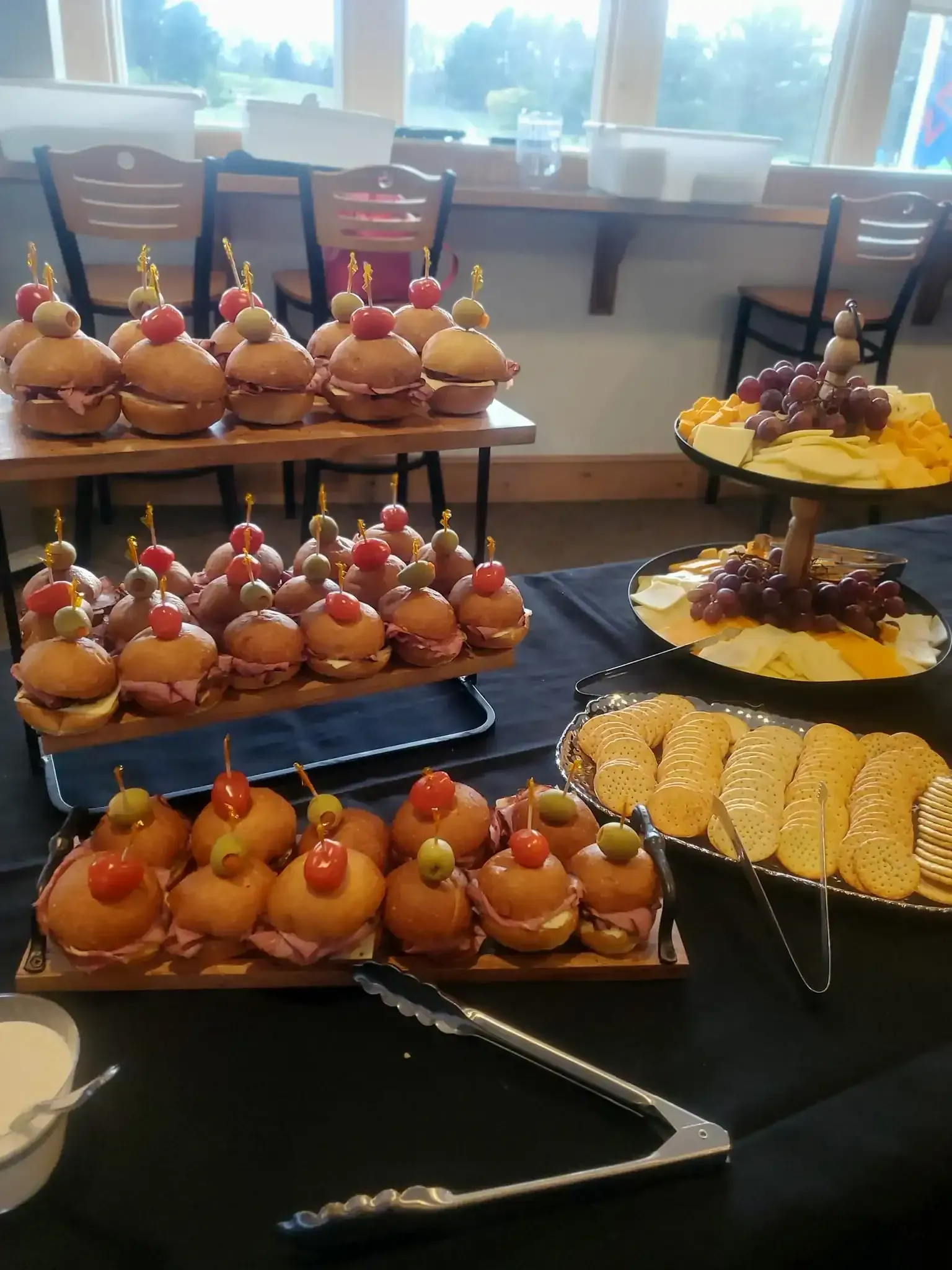 Dessert buffet on tiered trays with fruit tarts and pastries on a table near windows.