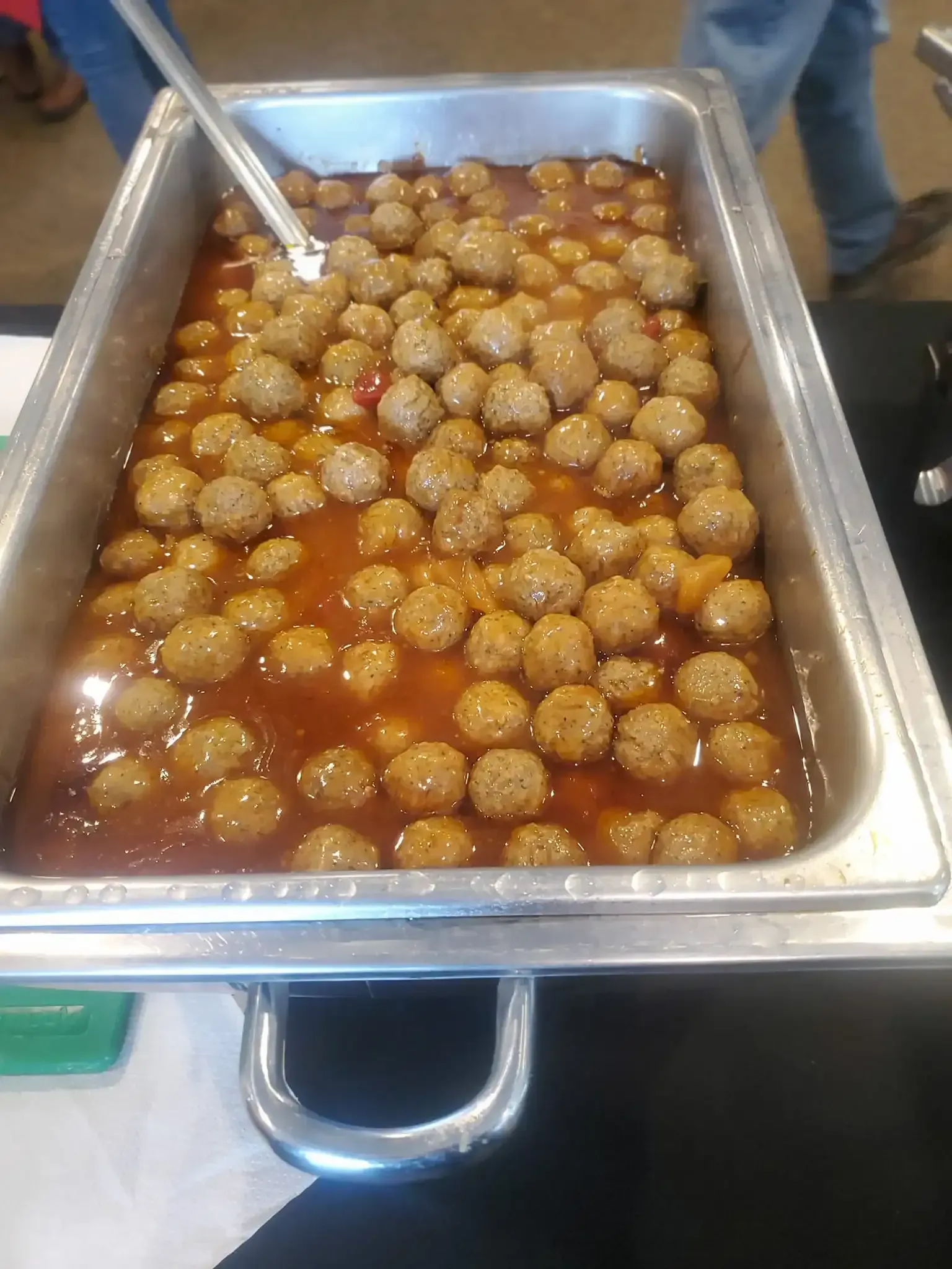 Tray of meatballs in red sauce, with a serving spoon in a buffet-style metal pan.