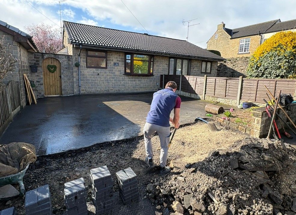 New tarmac driveway laid in front of a stone bungalow, with the ground prepared for a block paved entrance