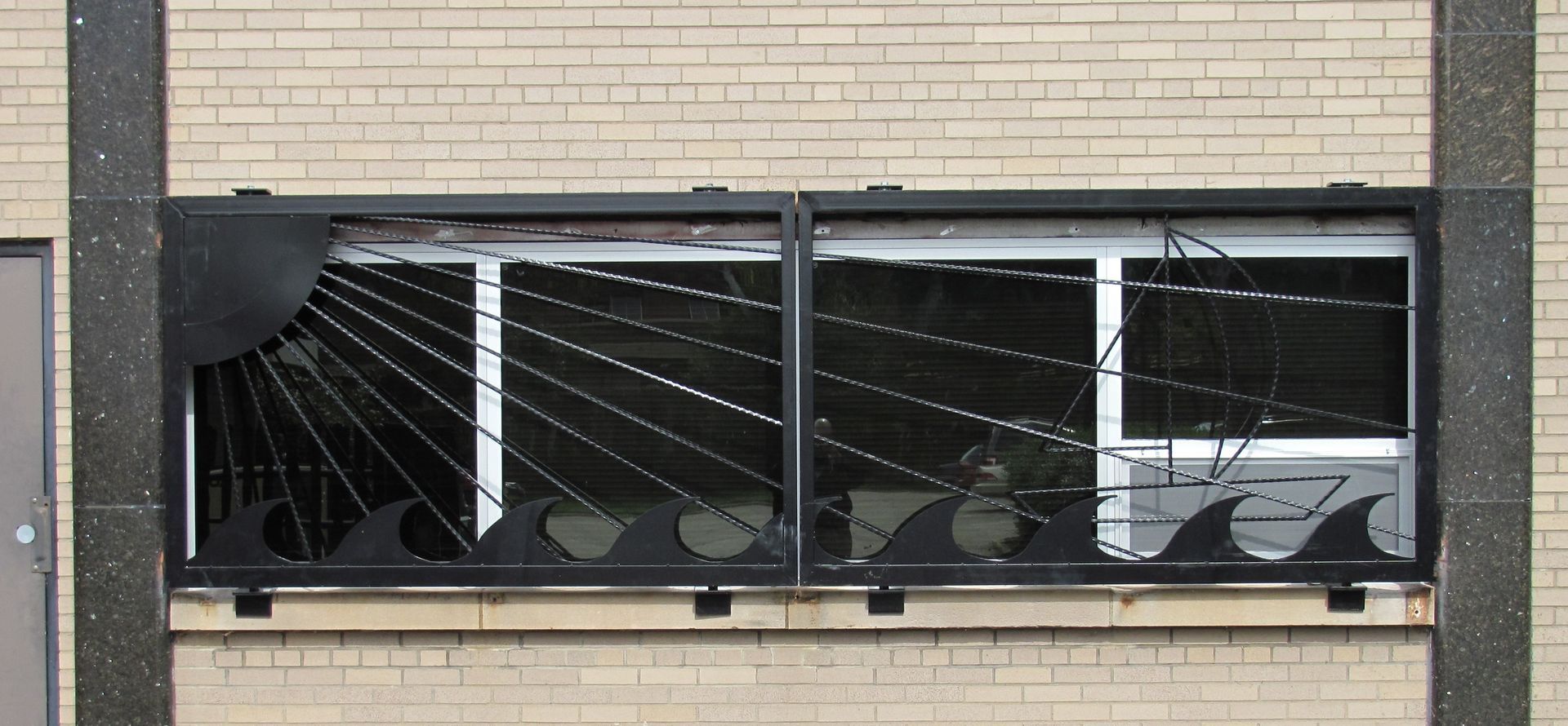 Window with black metal sun, waves, and boat designs on a brick building.