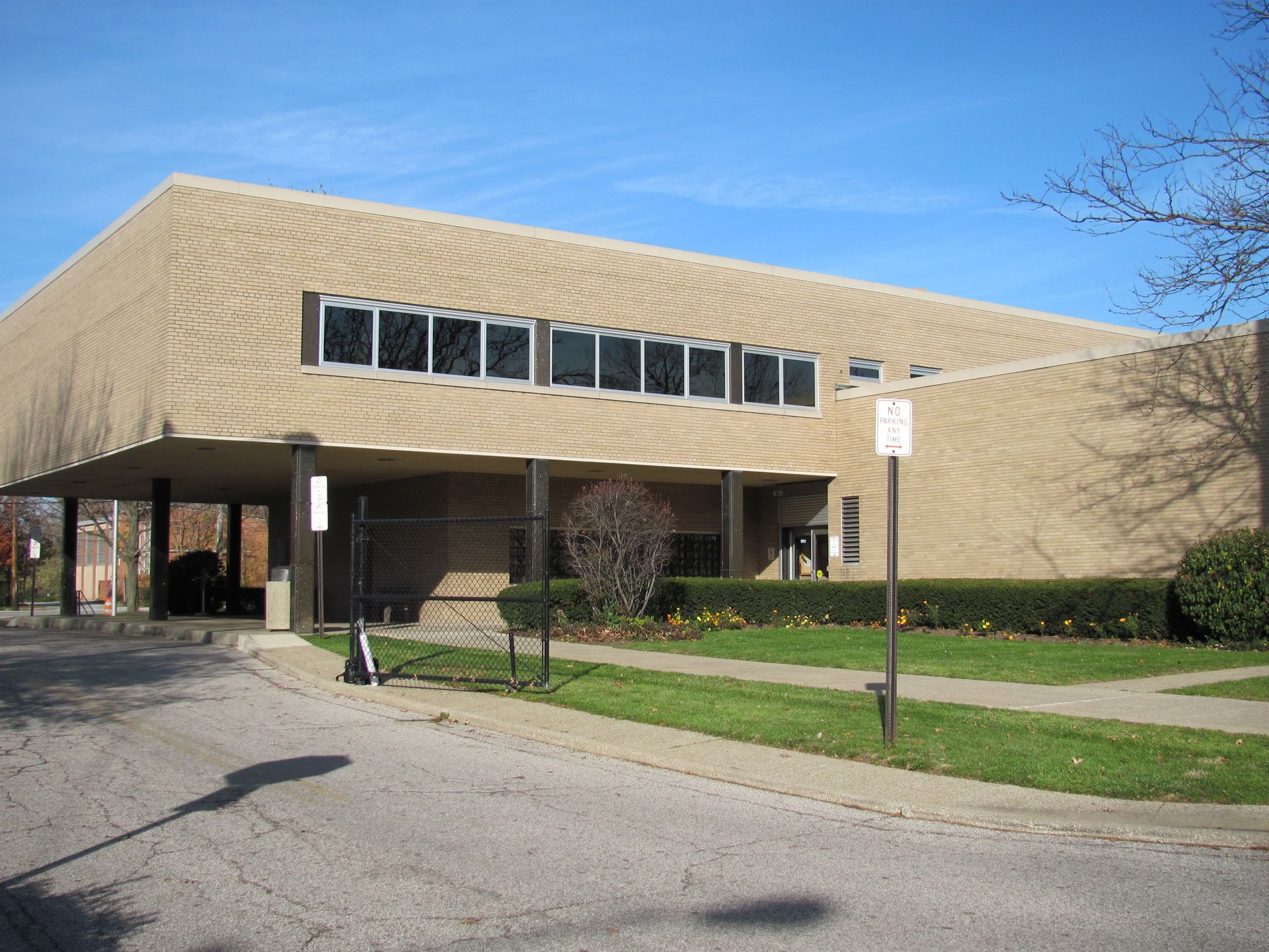 Tan brick building with a low overhang, featuring a row of small windows; sunny day.