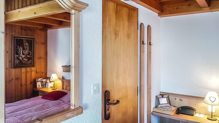 Chambre confortable avec boiseries, un lit et une porte en bois, se reflétant dans un grand miroir.