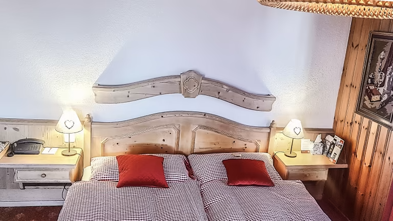 Chambre d'hôtel confortable avec deux lits jumeaux, oreillers rouges, tables de chevet avec lampes et tête de lit en bois.