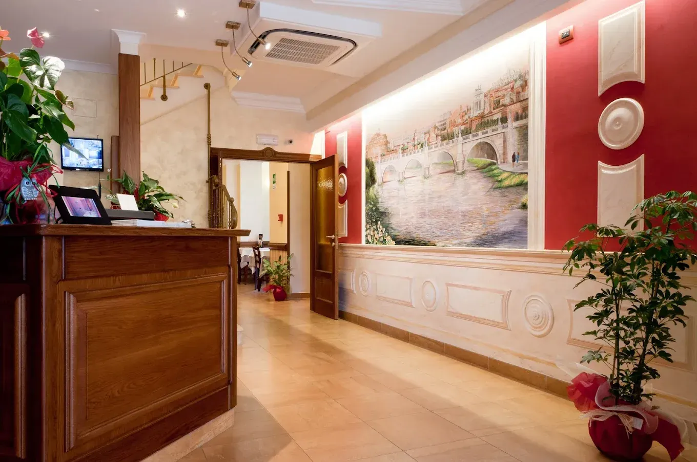 Accogliente hall d'albergo con bancone della reception in legno, pareti rosa, murale floreale e piante in vaso.