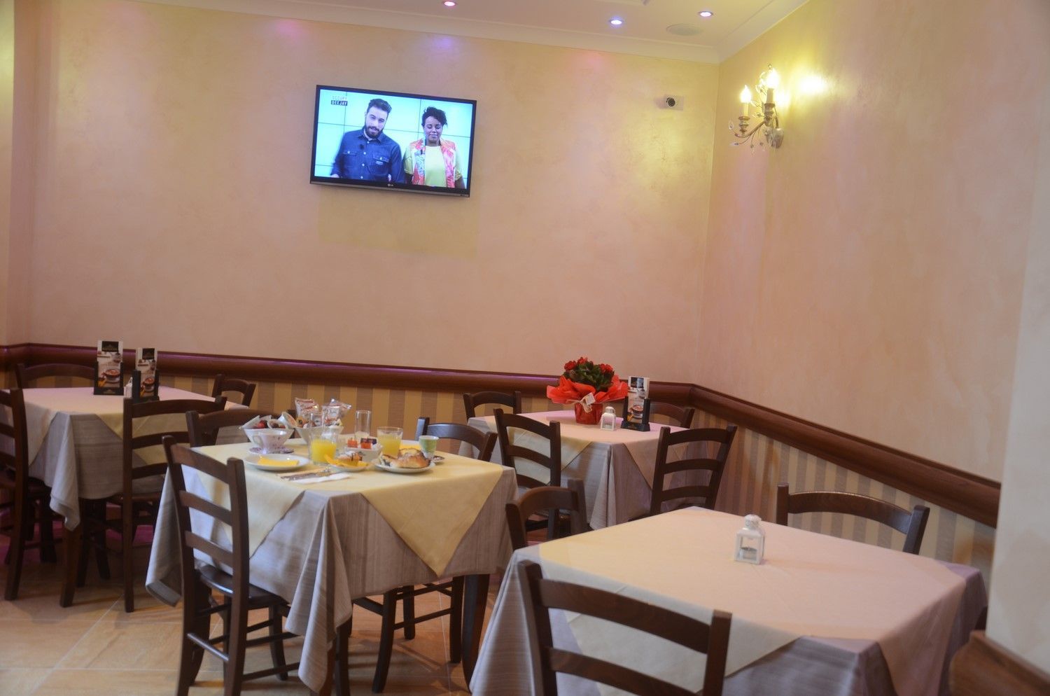 Piccola sala da pranzo di un ristorante con tavoli vuoti, sedie di legno e un televisore a parete.