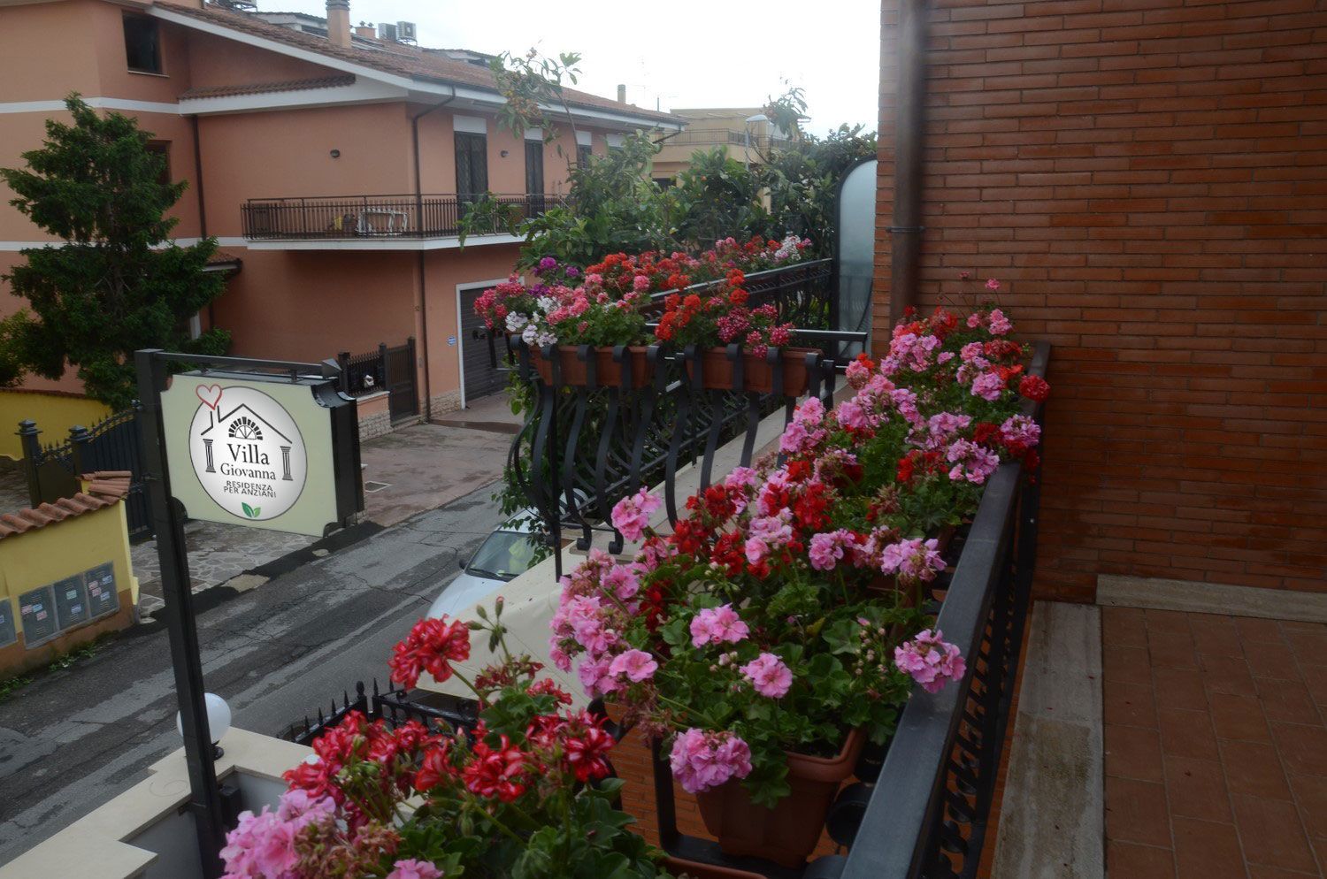 Balcone e cortile fioriti con vasi di fiori rosa e rossi accanto a edifici in mattoni.