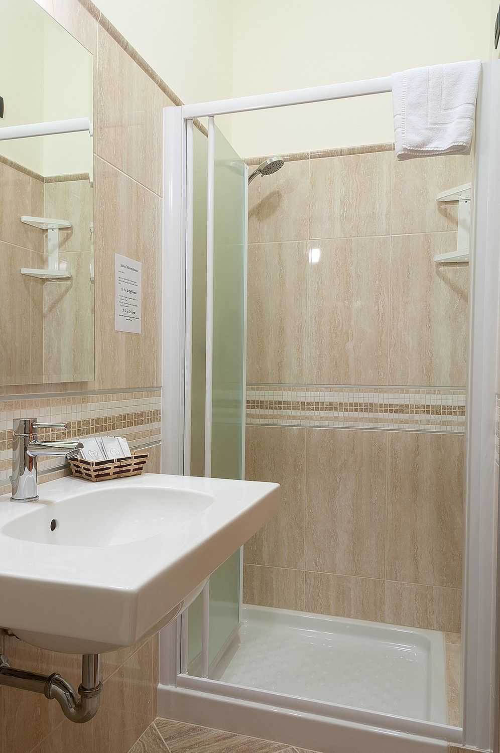 Piccolo bagno con lavandino, specchio e cabina doccia con piastrelle beige.