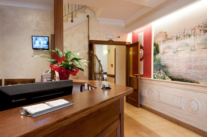 Bancone della reception nella hall dell'hotel con piano in legno, fiori rossi e murale.