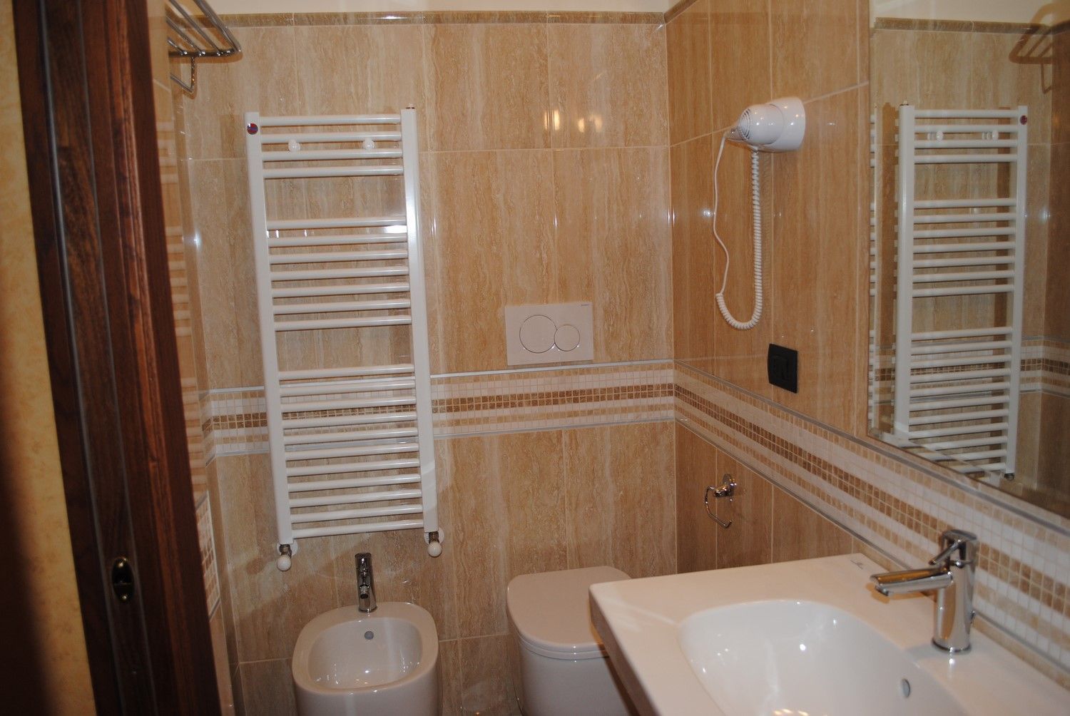 Piccolo bagno con piastrelle beige, lavabo, WC, doccia e termoarredo a parete.