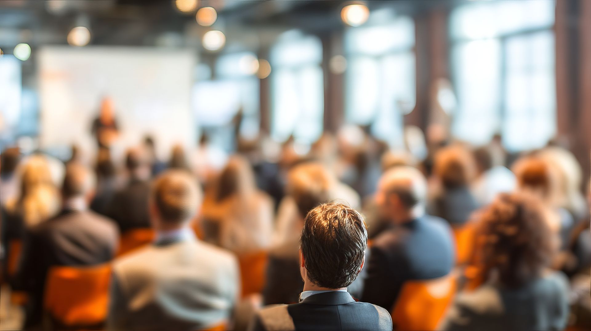 Vue floue prise derrière un public assistant à une présentation lors d'une conférence dans une salle moderne et lumineuse.