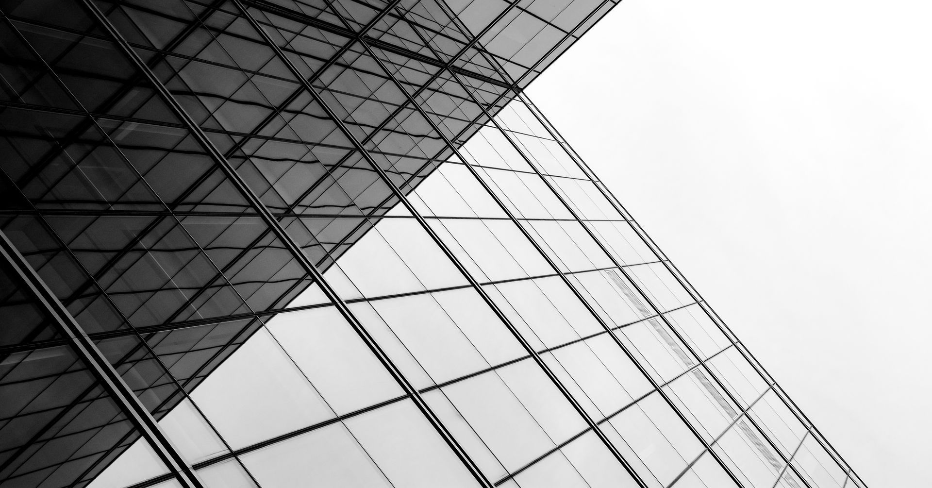Vue en contre-plongée, en noir et blanc, de la façade vitrée d'un gratte-ciel moderne, présentant des motifs géométriques en grille et des lignes nettes.