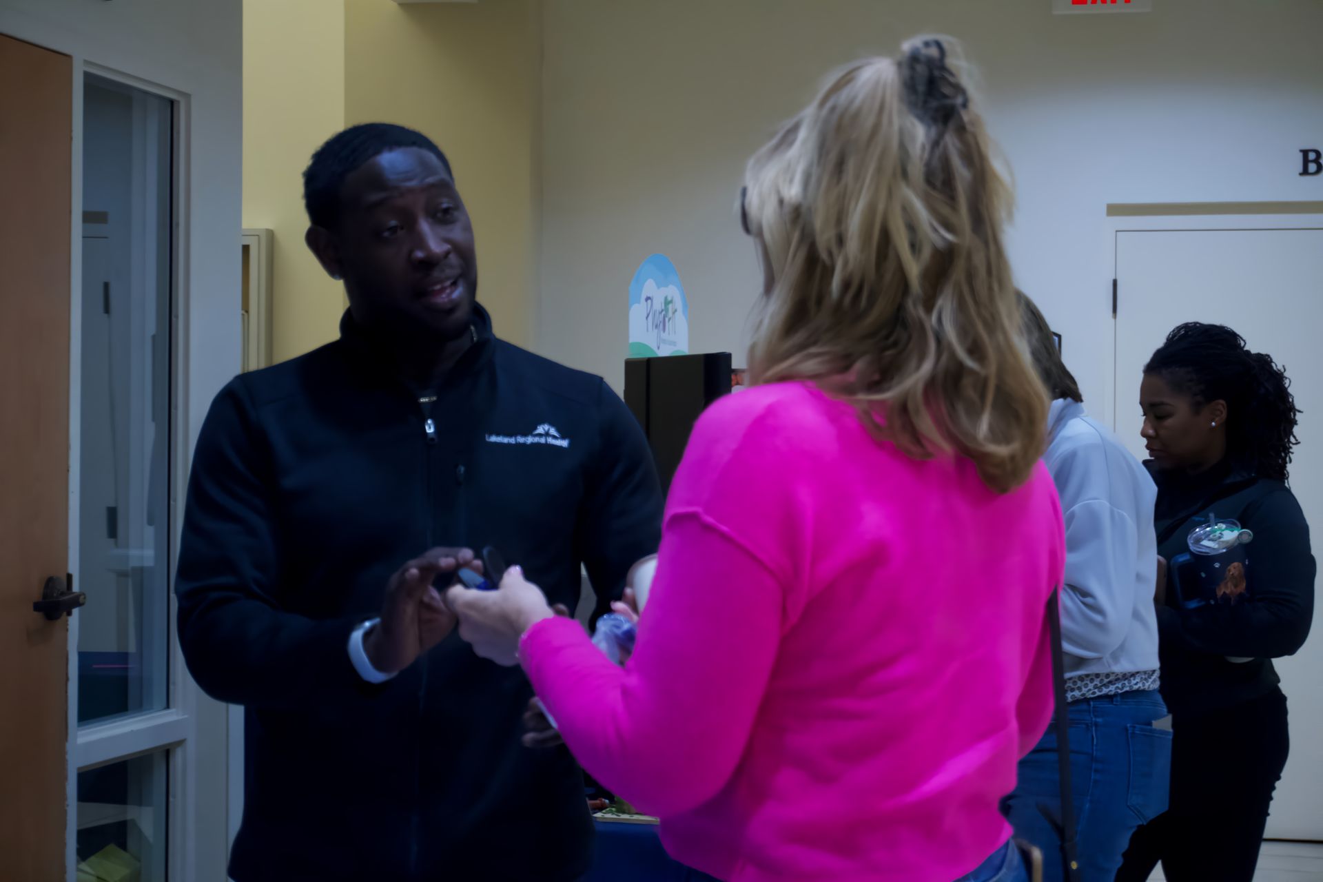 A man in a black jacket is talking to a woman in a pink sweater.