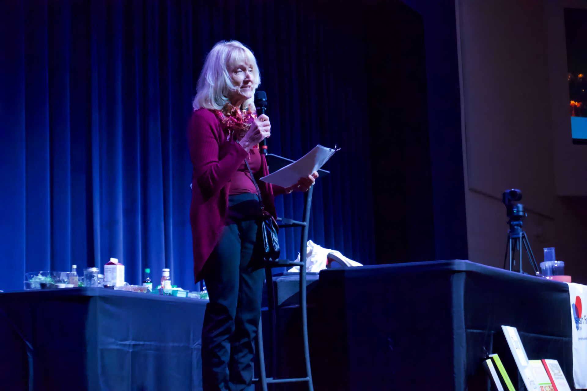A woman is standing on a stage holding a microphone and a piece of paper.