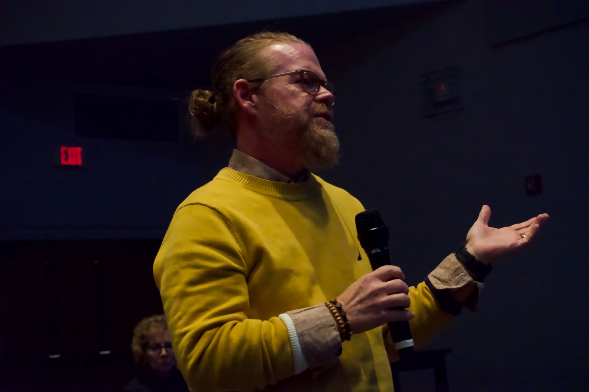 A man in a yellow sweater is speaking into a microphone.