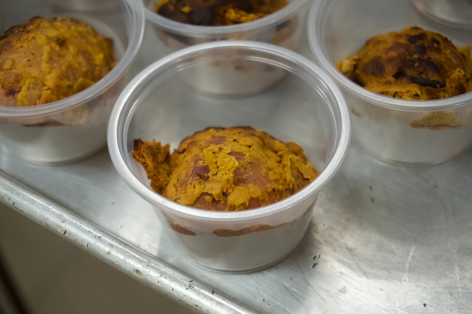 A bunch of plastic cups filled with food are sitting on a metal tray.