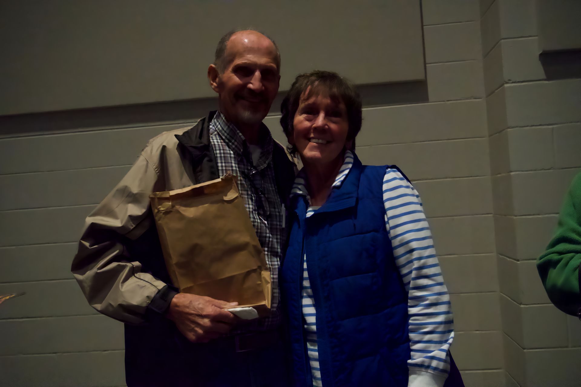 A man and woman are posing for a picture while the man is holding a brown bag