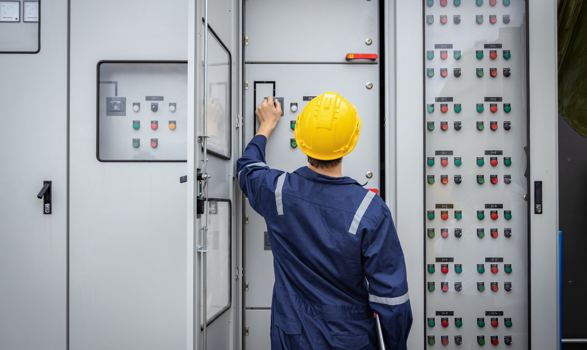 Electrician in blue uniform and yellow hard hat working on electrical panel. Electrician in blue uniform and yellow hard hat working on electrical panel.