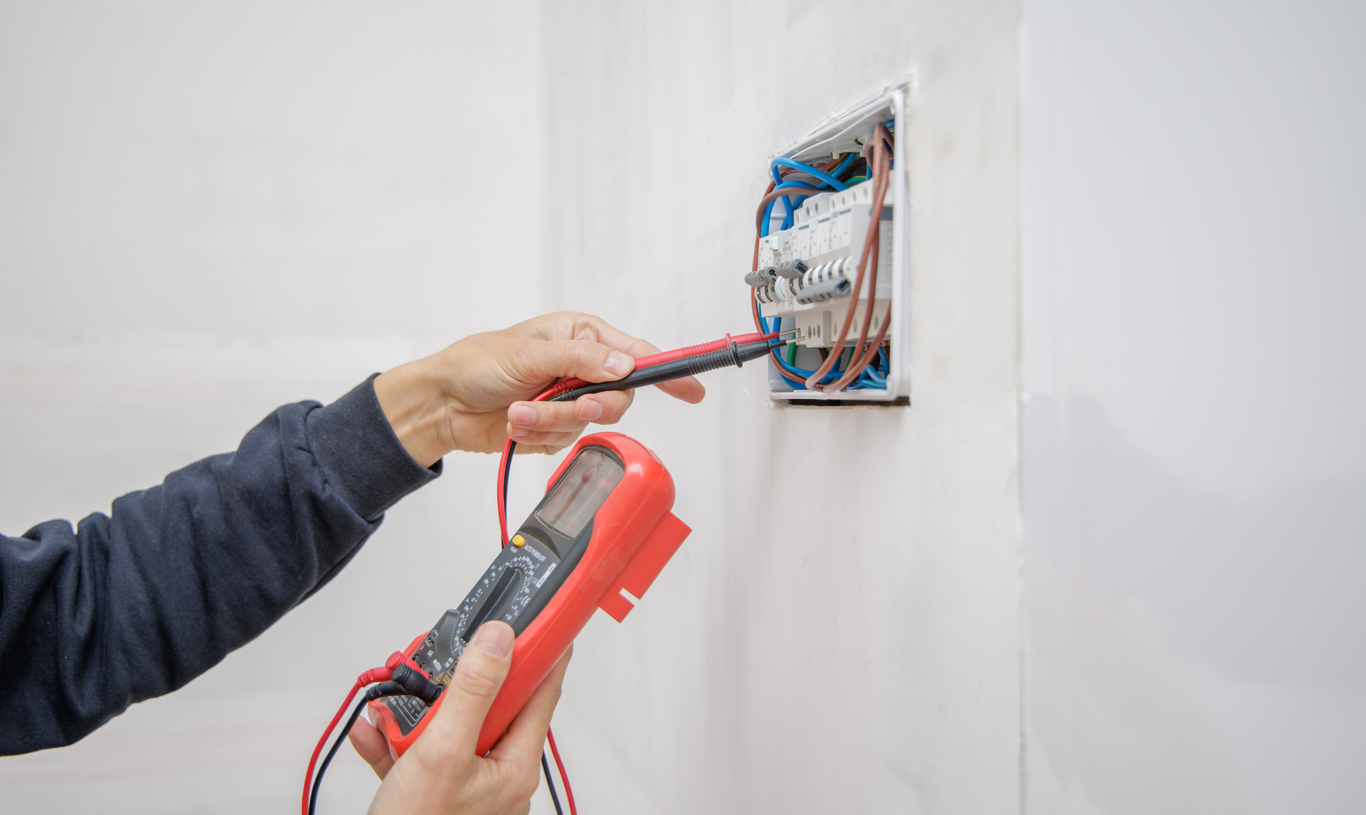 Person testing electrical wires in a wall outlet with a multimeter. Person testing electrical wires in a wall outlet with a multimeter.