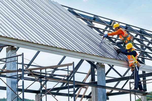 Roofers installing metal roof panels on a steel frame
