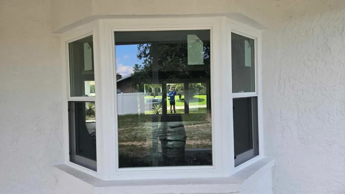 White bay window on a stucco wall reflecting trees and a yard outdoors