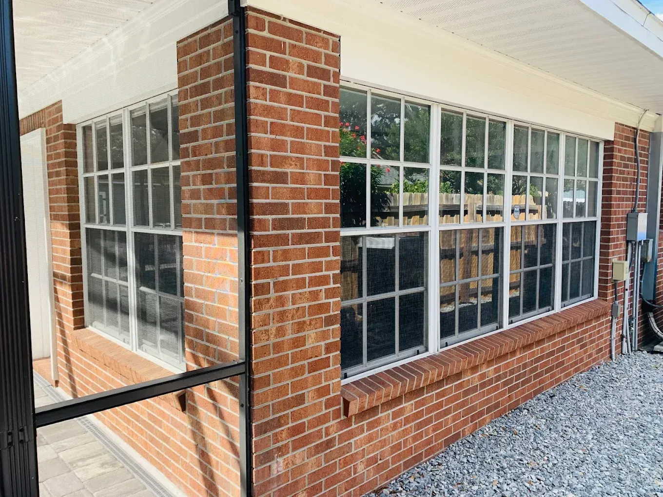 Brick building corner with large white-trimmed windows and a gravel walkway