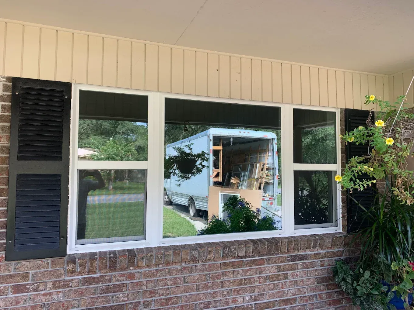 White-framed windows in a brick-and-beige house exterior, reflecting trees and a covered patio.