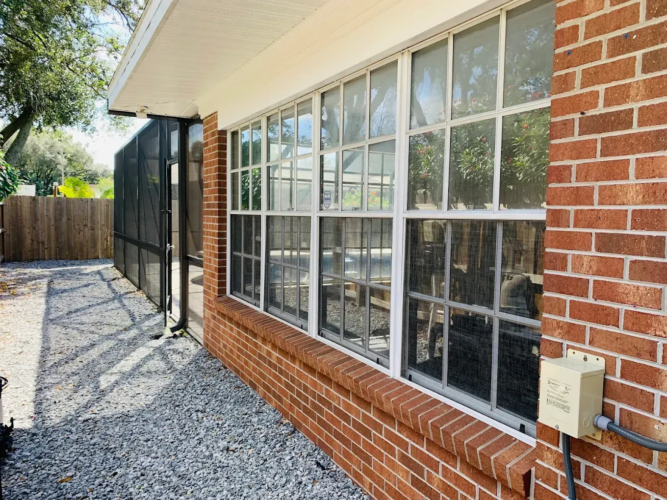 Brick house side exterior with large windows, gravel path, and fenced backyard area