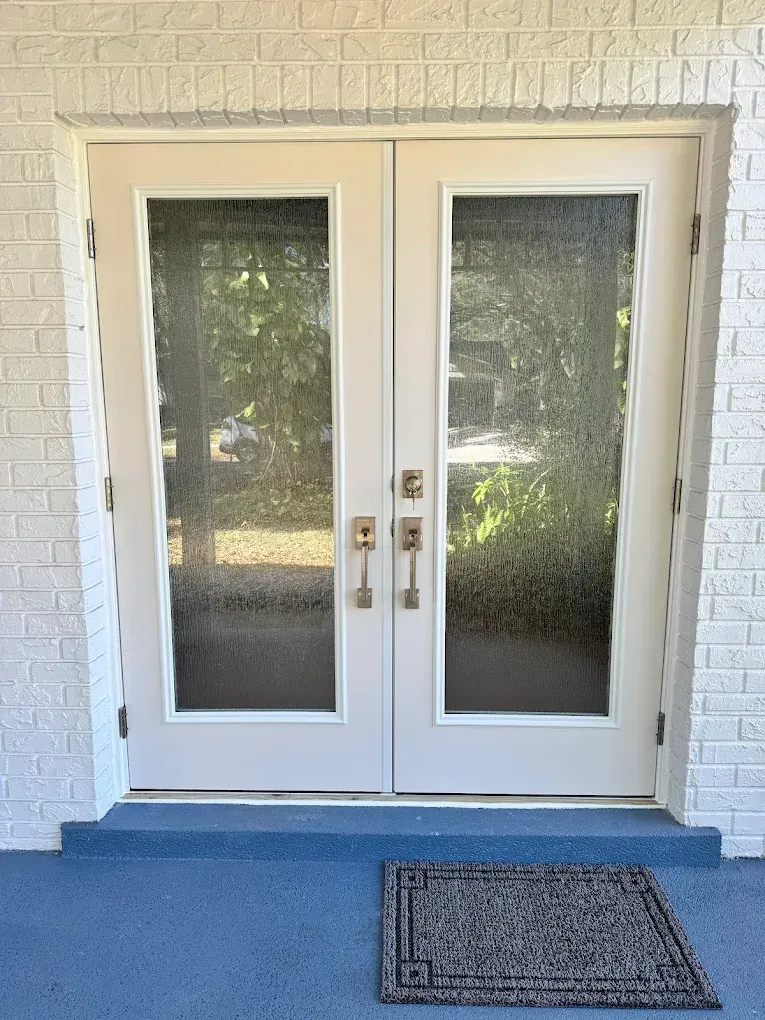 White double glass doors with brass handles and a blue step, viewed from outside.