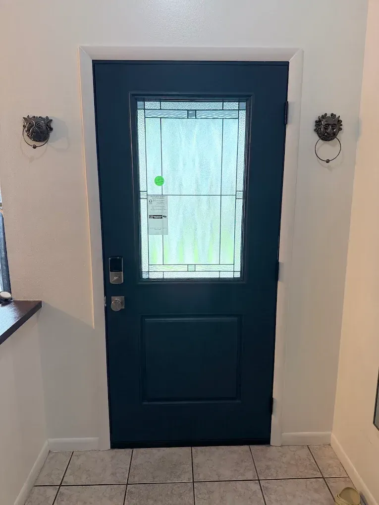 Dark front door with glass pane, flanked by wall sconces over a tiled entryway.