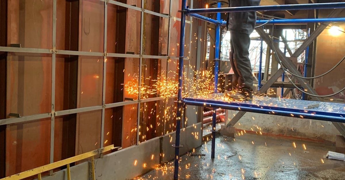 Construction worker cutting metal rebar with sparks flying on a wet scaffolded site