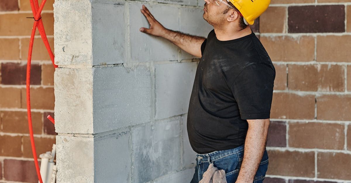 Construction worker in yellow hard hat inspecting a cinder block wall inside a building.