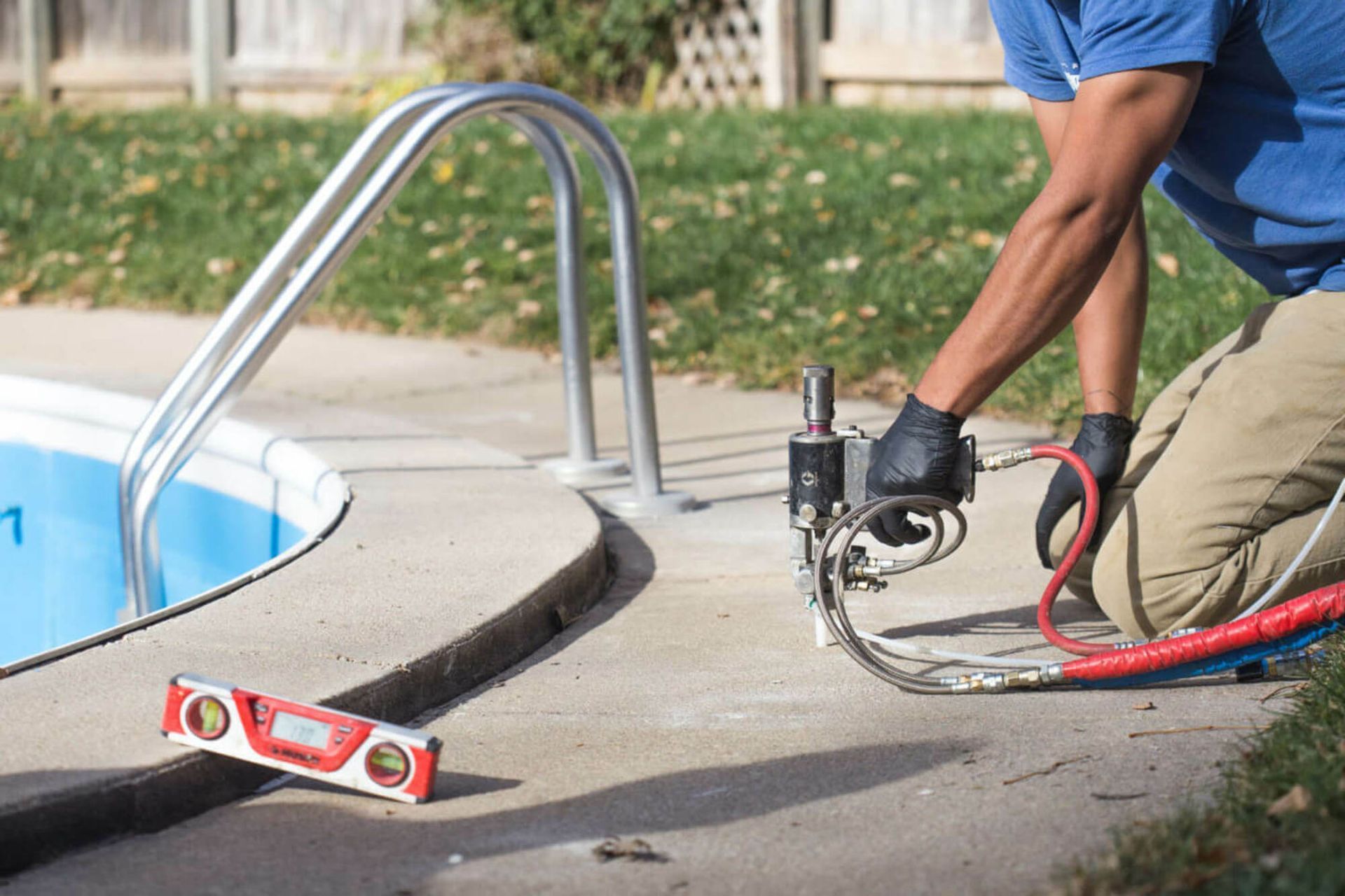 Worker using a circular saw to cut concrete beside a swimming pool