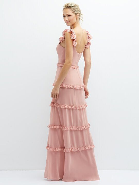 Woman in a pink ruffled tiered gown standing in profile against a plain white background
