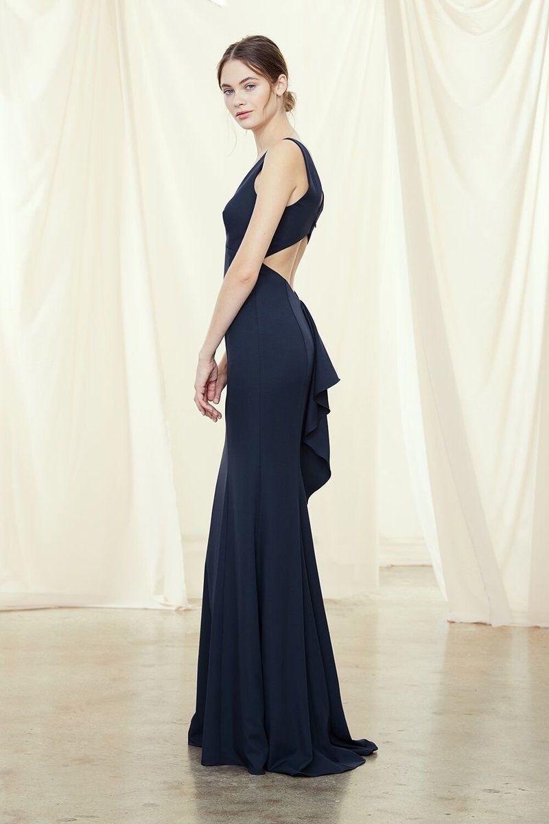 Woman in a navy gown posing against a cream draped backdrop