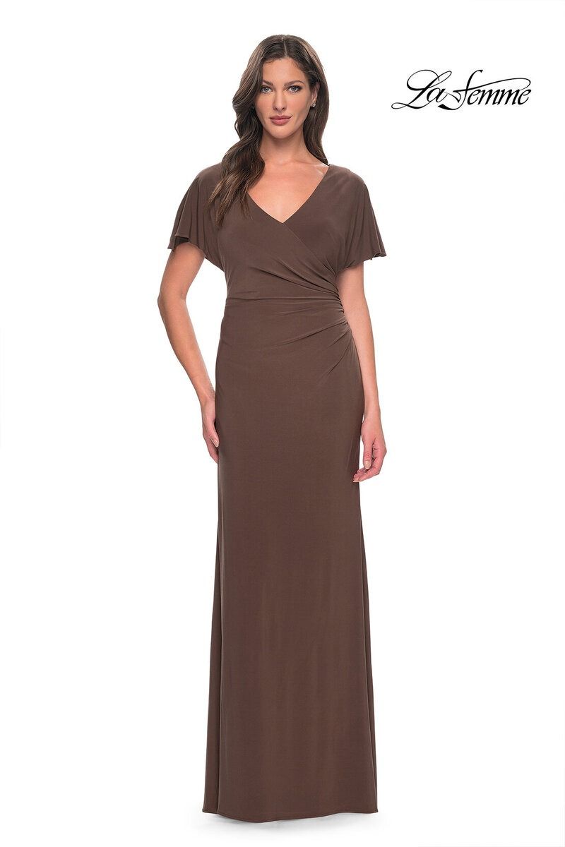 Woman in a long brown wrap dress standing against a white background.
