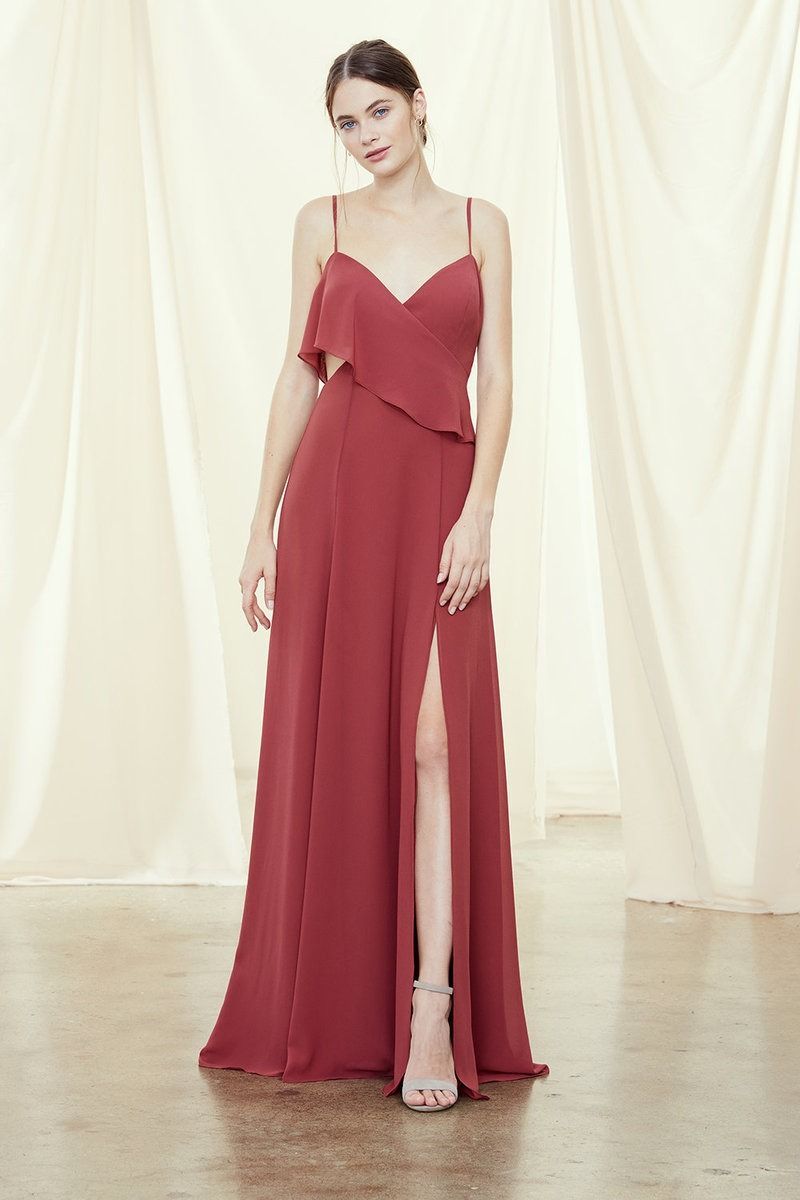 Woman in a red floor-length gown standing on a studio floor before cream curtains