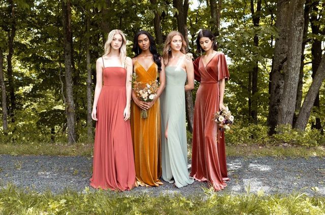 Four women in flowing dresses standing together outdoors in a wooded garden