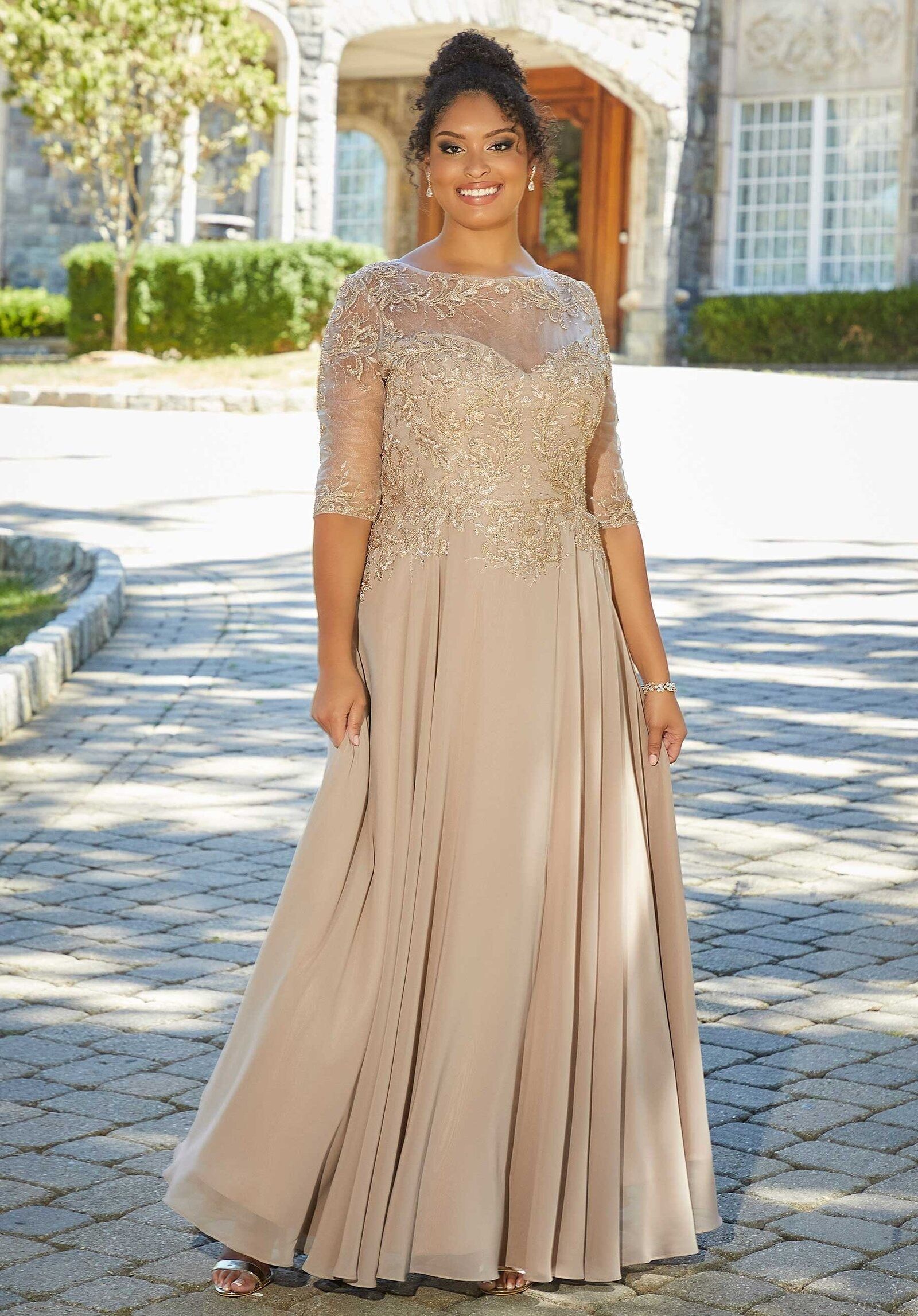 Woman in a sparkling beige gown standing outdoors on a sunlit path.
