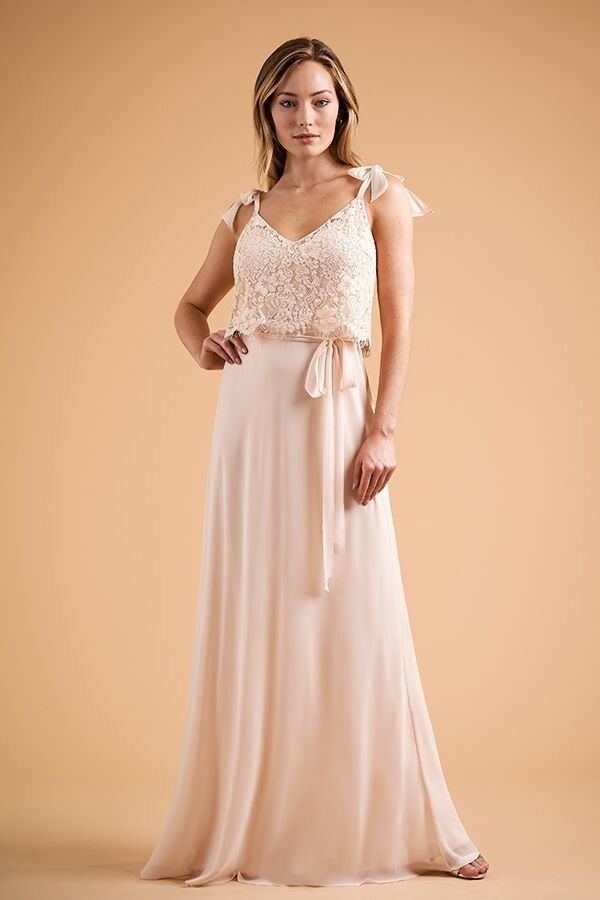 Woman in a blush lace maxi dress standing against a peach background.