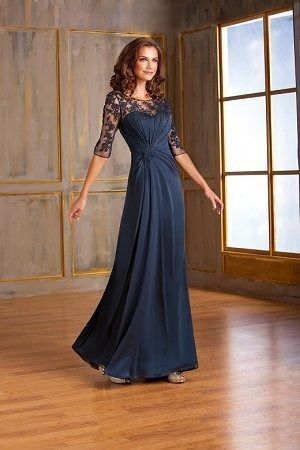 Woman in a navy lace evening gown standing in a sunlit room by tall windows