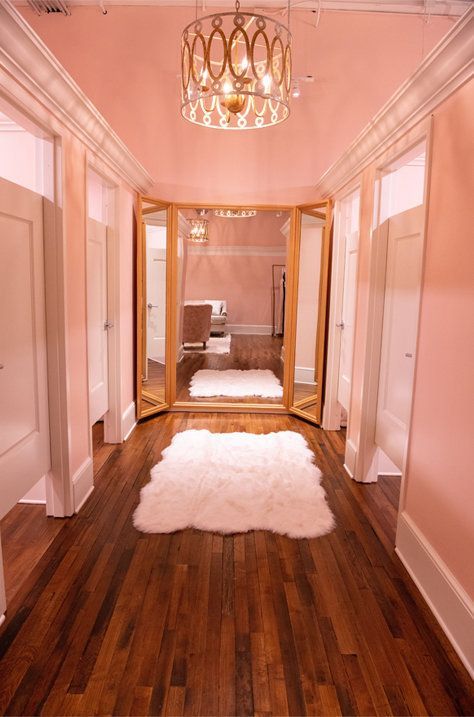 Pink hallway with wood floors, gold chandelier, and white rugs leading to a bedroom through mirrored doors